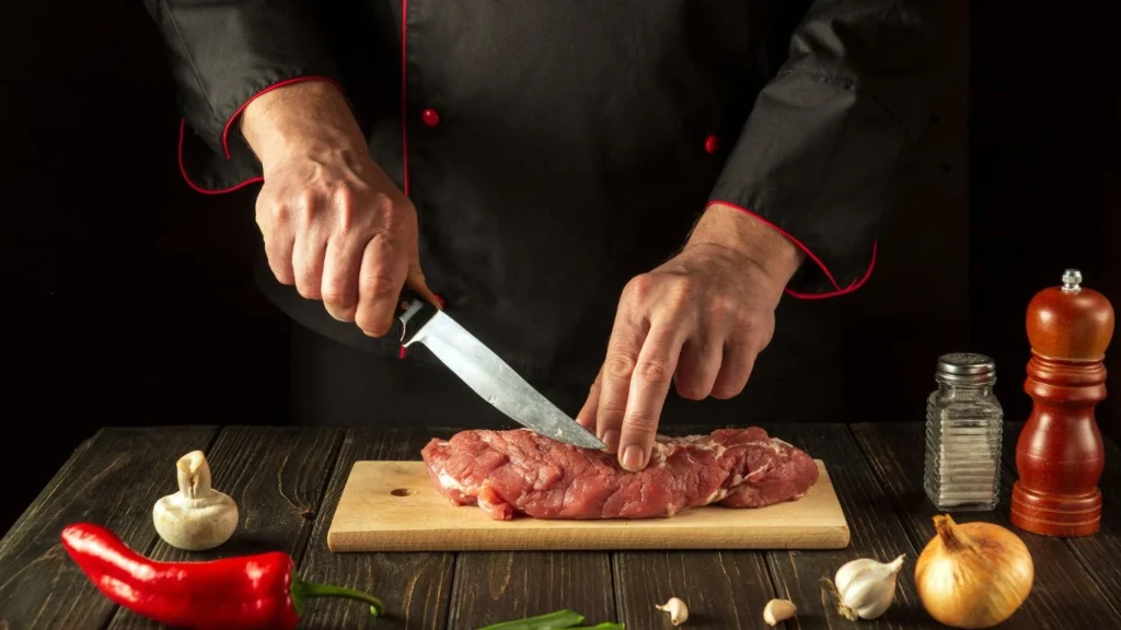 Assorted raw beef cuts displayed on a wooden board, labeled with names like ribeye, sirloin, tenderloin, and flank, showcasing marbling and texture differences