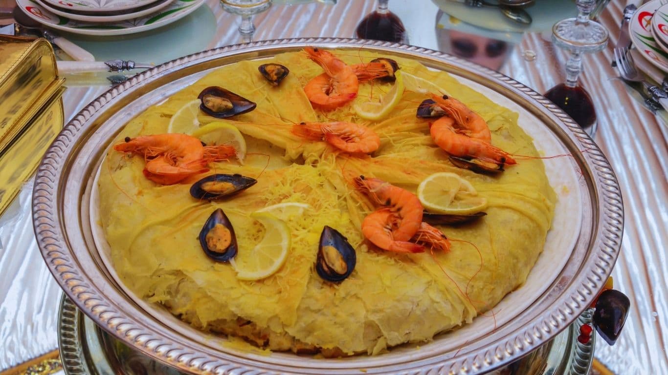 Moroccan Seafood Bastilla with golden crispy phyllo pastry filled with spiced seafood and vermicelli, garnished with fresh herbs and lemon slices.